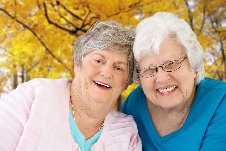 Two elderly women smiling in an autumn setting.