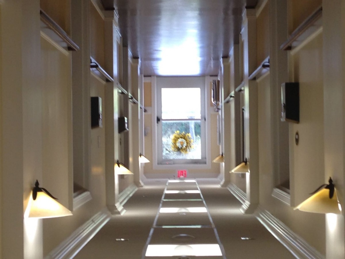 A brightly lit hallway with symmetrical windows and a distant view through a large window at the end.