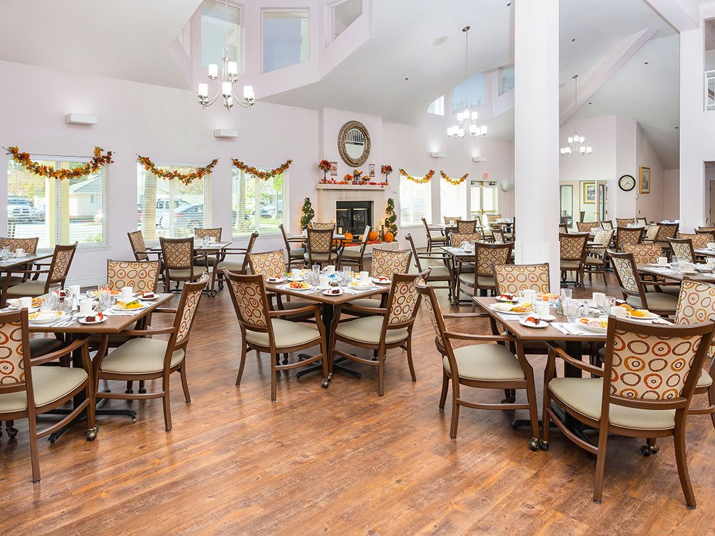 A spacious dining area with elegant decor, featuring multiple tables and chairs arranged on a wooden floor.