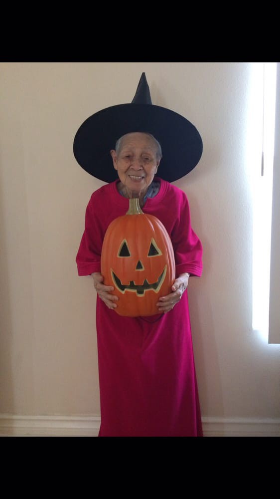 A person dressed in a witch costume holding a carved pumpkin indoors, smiling at the camera.