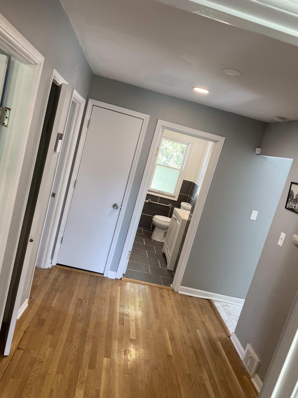 A hallway with hardwood flooring leading to a bathroom.