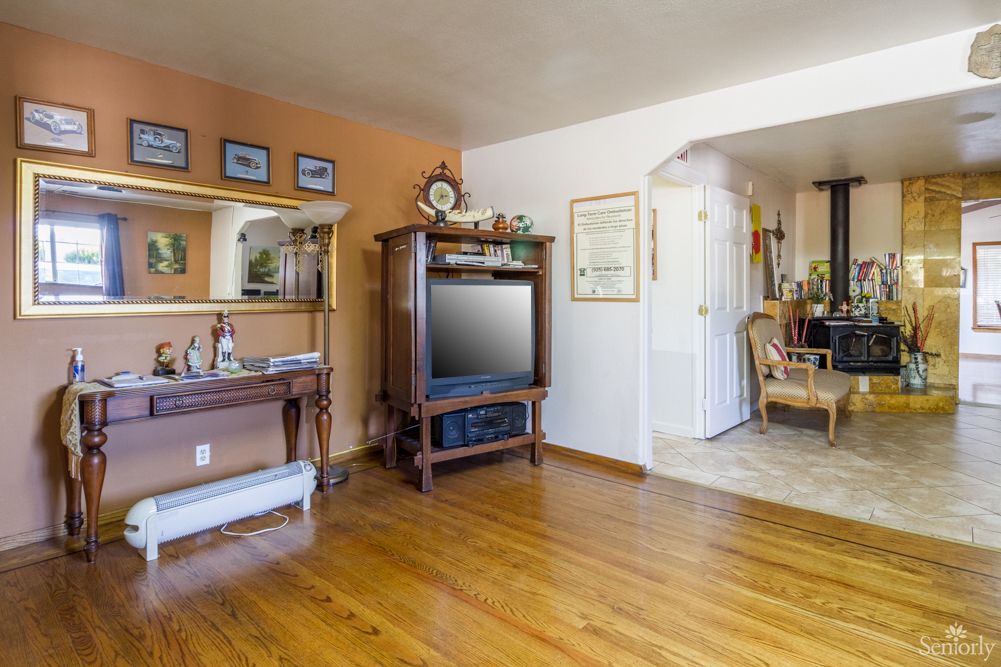 A cozy living room with wooden flooring, featuring a television and elegant furniture, leading to an open archway into another area.