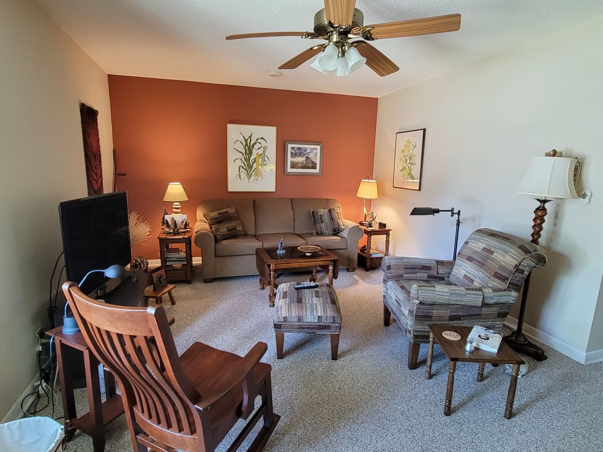 A cozy living room with a sofa, armchair, ceiling fan, and artwork on the walls.