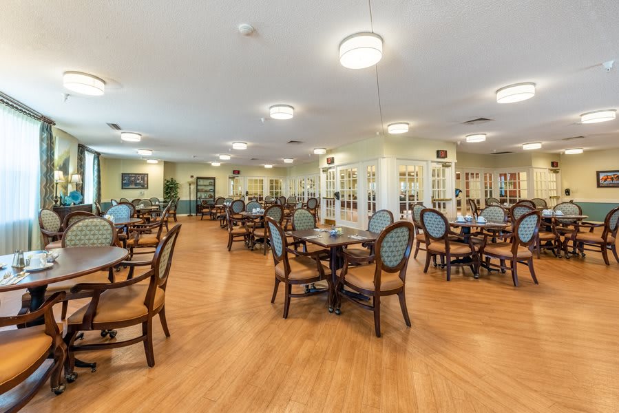 A spacious dining area with several tables and chairs on a wooden floor.
