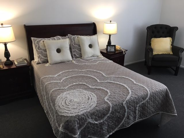 A neatly made bed with a patterned quilt and decorative pillows, accompanied by a bedside lamp in a cozy bedroom setting.