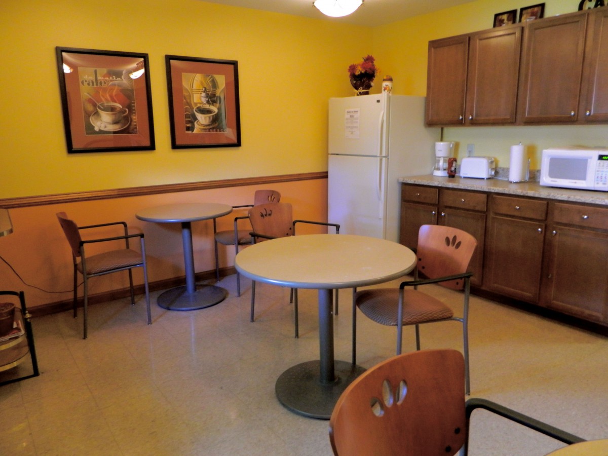 A cozy kitchen and dining area with tables, chairs, a fridge, and colorful artwork on the walls.