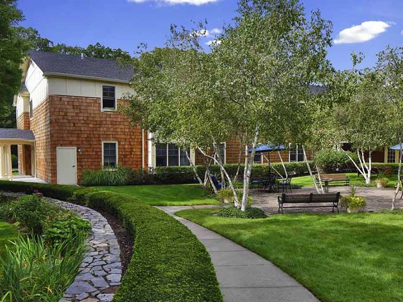 A charming house with a beautifully landscaped garden featuring a walkway, lush lawn, trees, and outdoor seating.