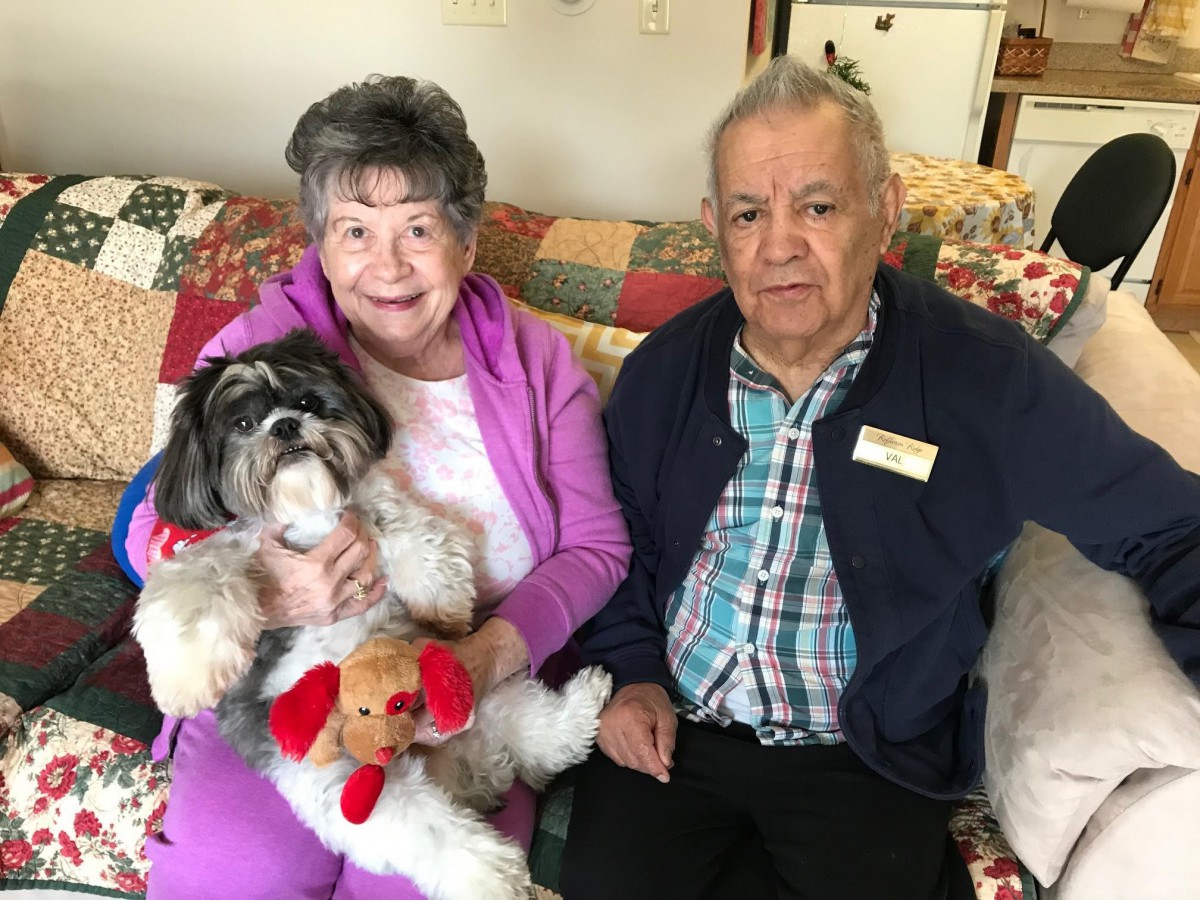 An elderly couple sitting on a couch with their small dog.