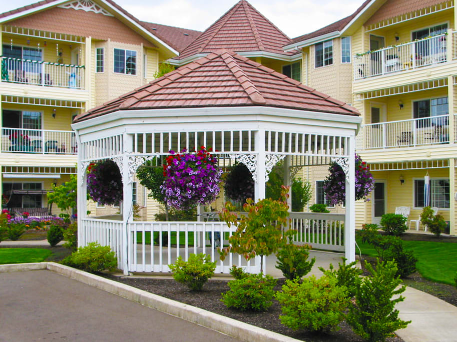 A beautifully decorated gazebo with hanging flowers in a garden setting, surrounded by residential buildings.