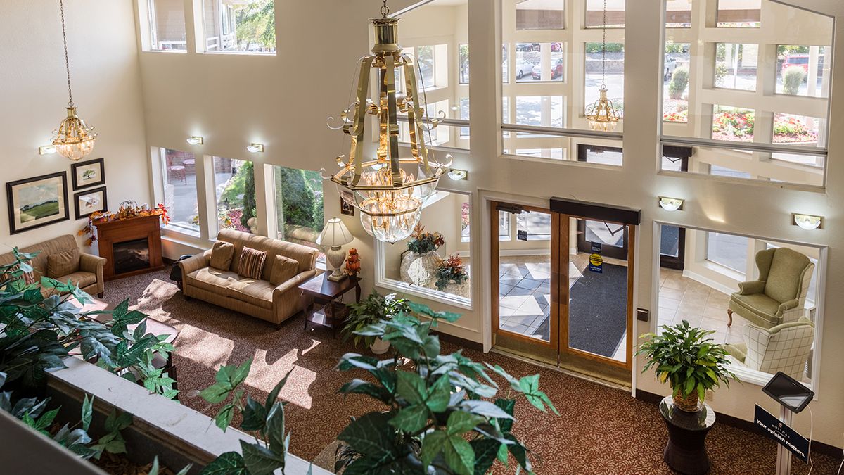 A spacious and well-lit lobby featuring a grand chandelier, comfortable seating, and lush indoor plants.