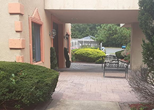 A view of a pathway leading to a building, featuring well-maintained greenery and a bench.