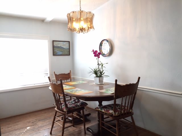 A cozy dining area with a wooden table and chairs, an orchid centerpiece, and a chandelier casting warm light.