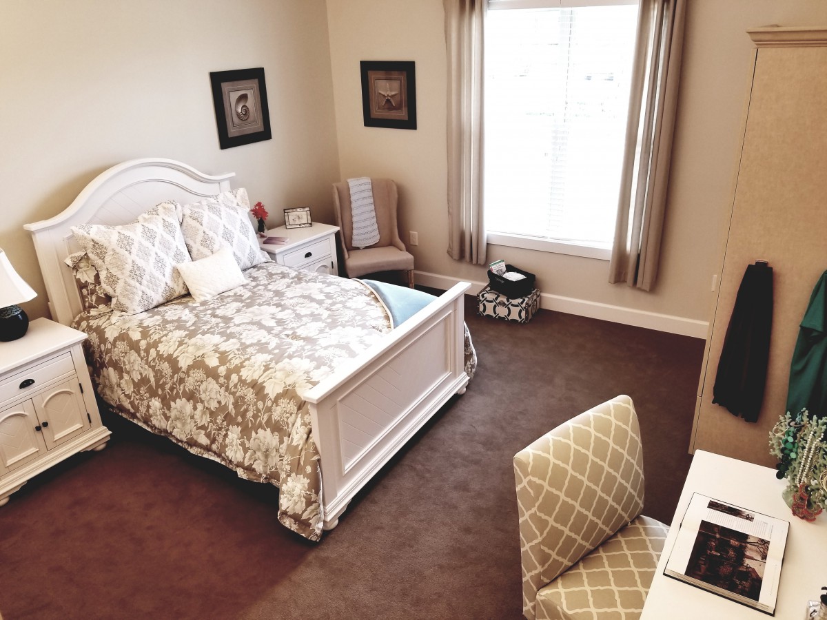 A cozy and well-decorated bedroom with a bed, nightstand, and a window letting in natural light.