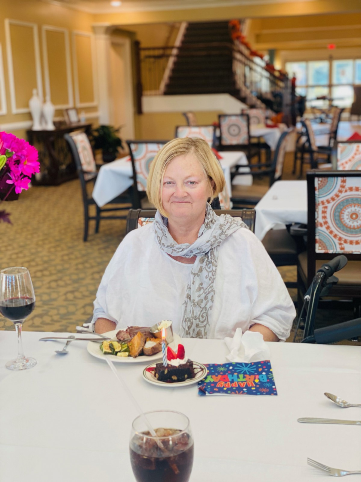 A woman enjoying a birthday meal at a restaurant with cake and wine.