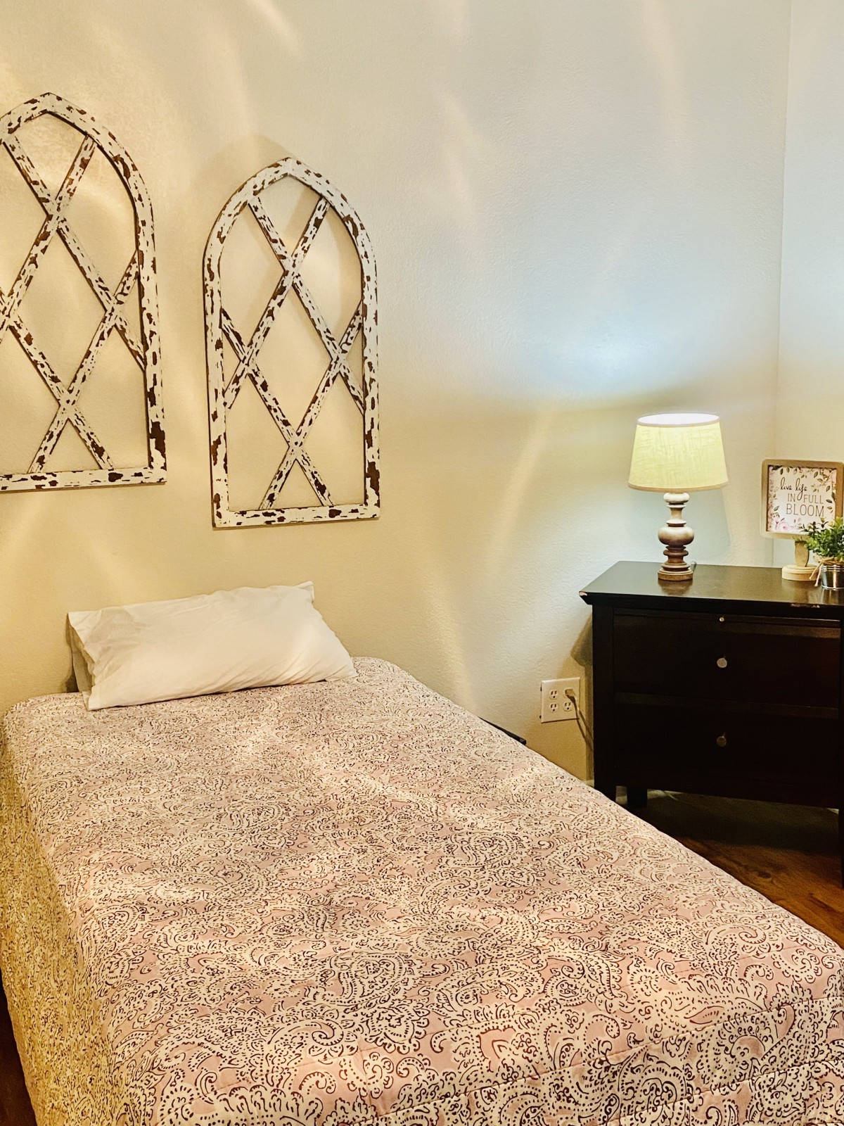 A cozy bedroom with a single bed and nightstand, featuring decorative wall art and a lit lamp.