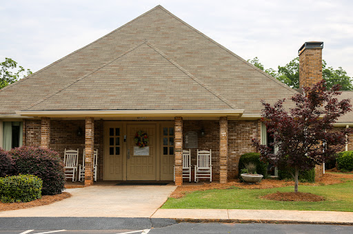 A cozy building with a welcoming entrance and outdoor seating surrounded by greenery.