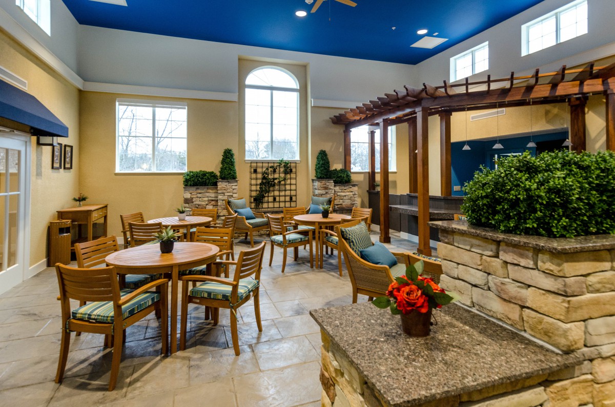 A well-lit interior dining area featuring wooden tables and chairs, accented by greenery and decor elements.