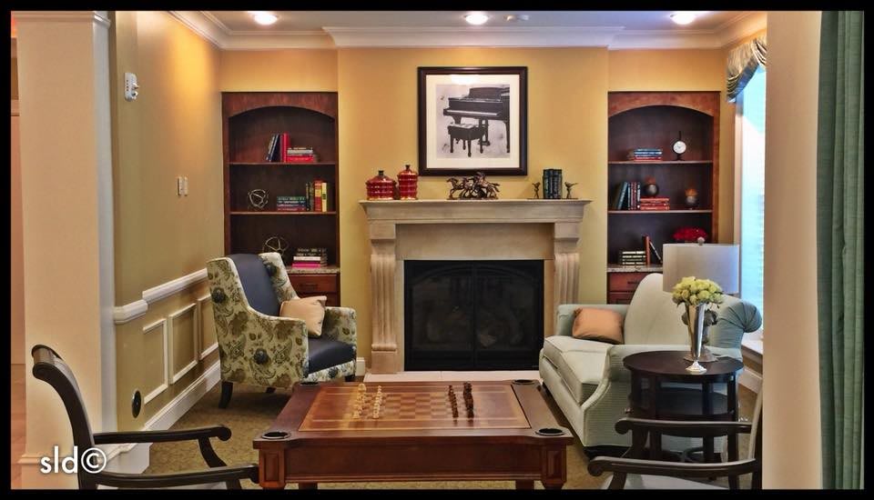 A cozy living room with a fireplace, surrounded by bookshelves and comfortable seating.