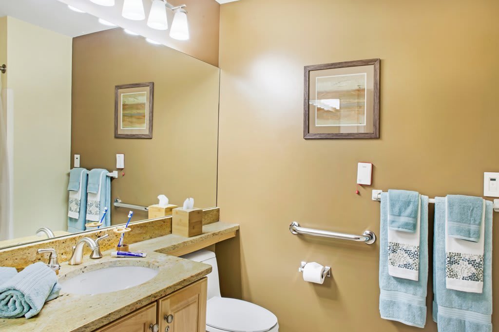 A neatly organized bathroom with a mirror, sink, toilet, towel rack, and wall art.