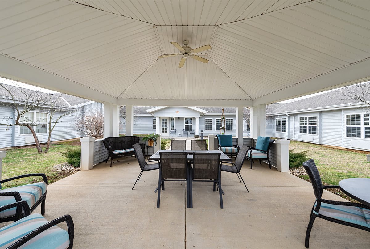 A cozy outdoor gazebo with a dining table, chairs, and comfortable seating set under a ceiling fan.
