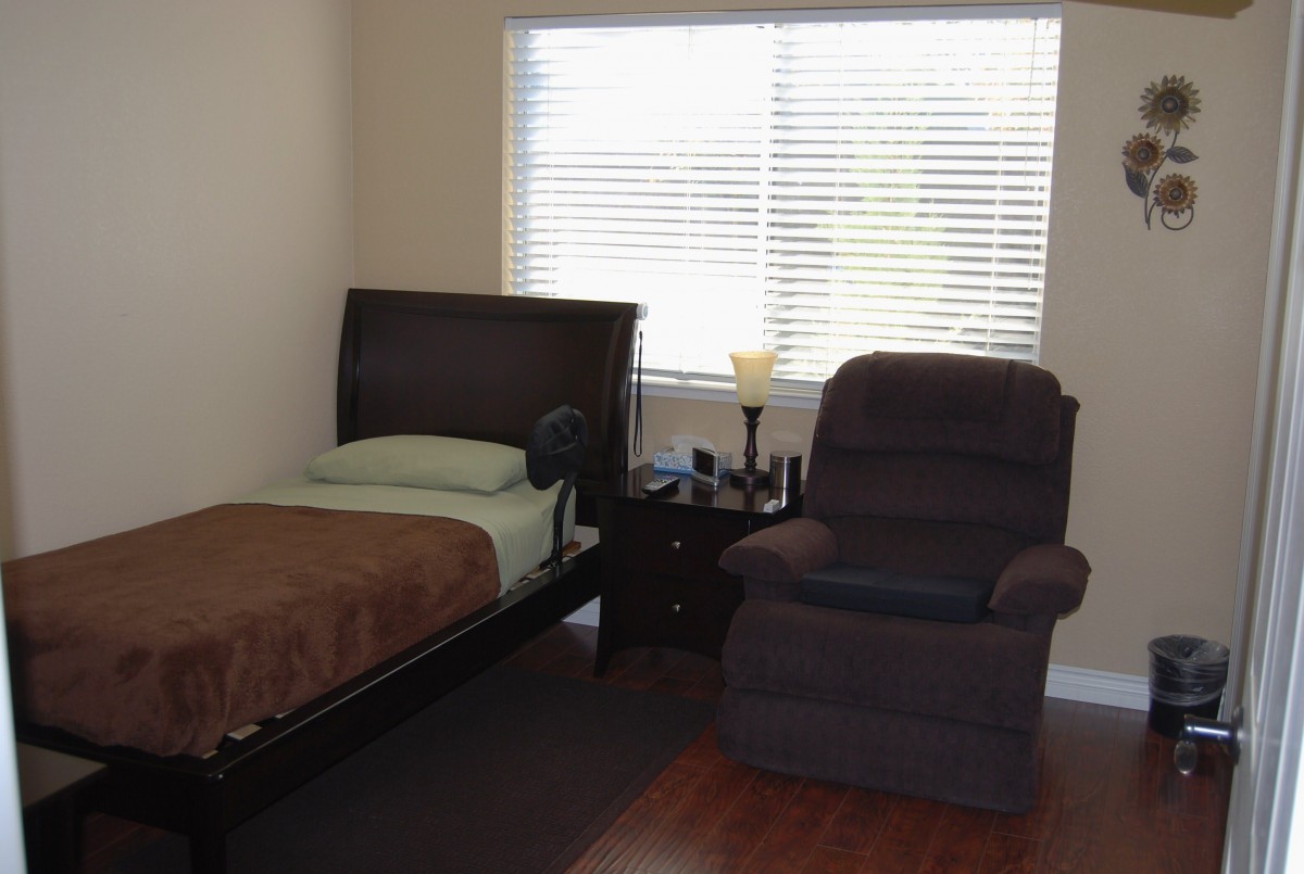 A simple bedroom with a single bed, recliner, and a window with blinds.