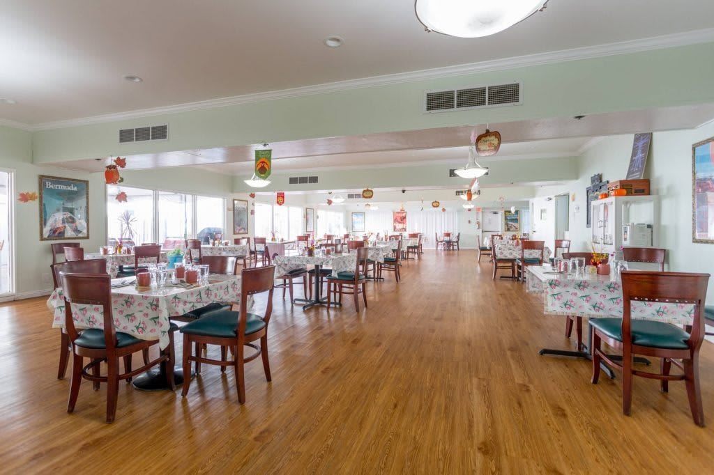 A spacious dining area with neatly arranged tables and chairs on a wooden floor.