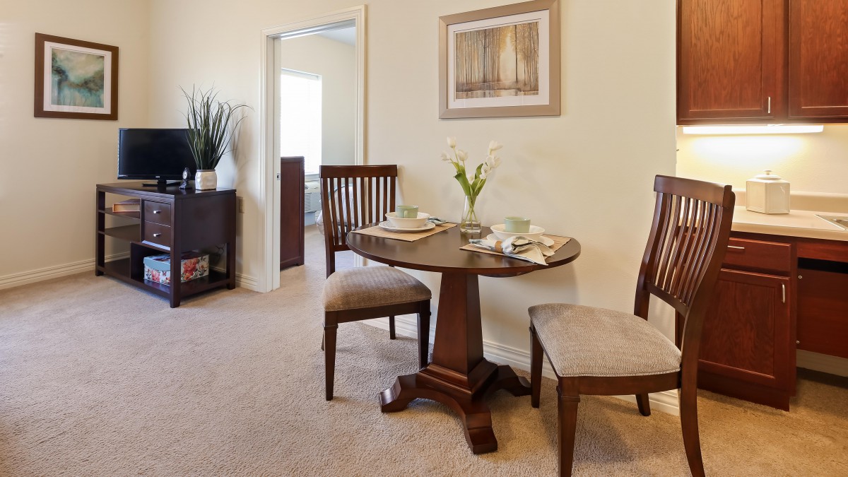 A cozy dining area featuring a small round table set for two with elegant chairs, adorned with a vase of flowers and artwork on the wall.