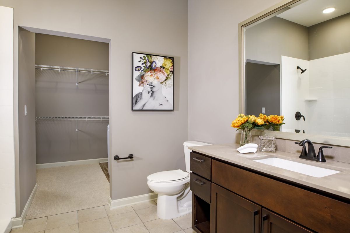 A modern bathroom with a large mirror, wooden vanity, and decorative artwork on the wall.