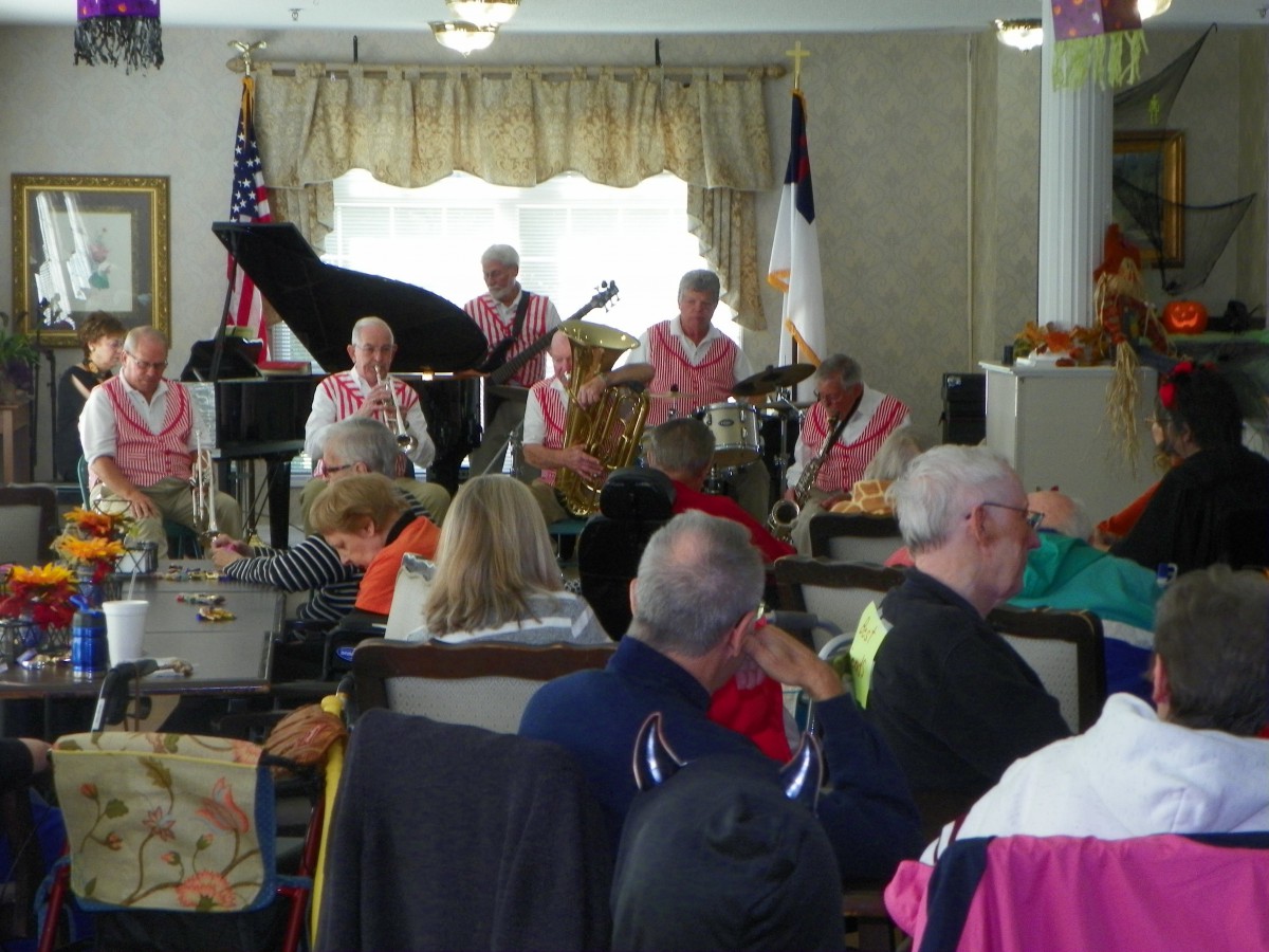 A band performs for an audience at a community event, featuring musicians playing various instruments in an indoor setting.
