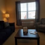 A cozy living room featuring a sofa, armchair, lamp, and a coffee table in front of a large window.