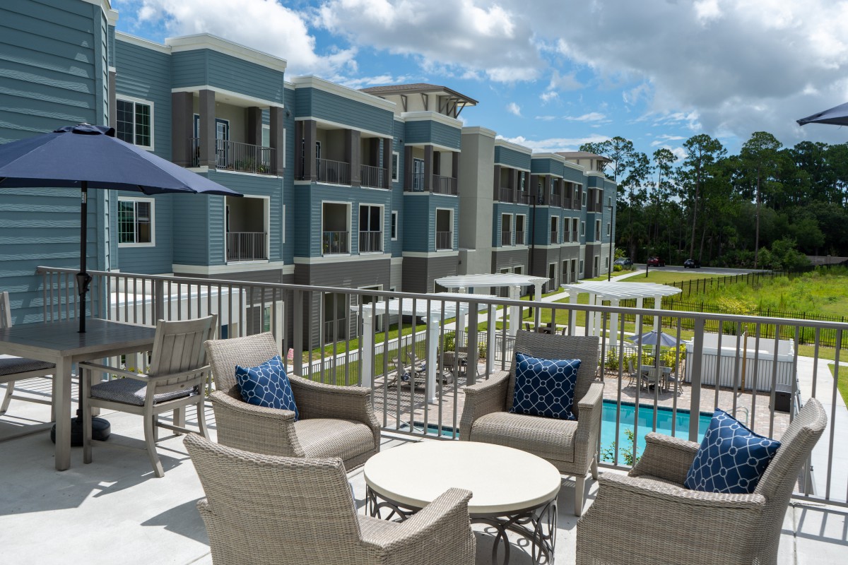 A modern apartment complex with outdoor seating and a pool area on a sunny day.