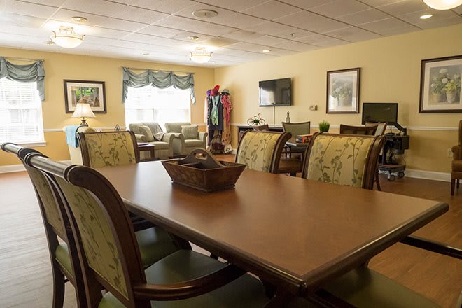 A spacious dining room with a large wooden table and chairs, featuring cozy decor and natural lighting from a window.