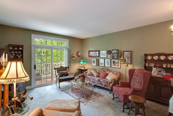 A cozy living room with comfortable furniture, decorated with artwork and large windows overlooking greenery.