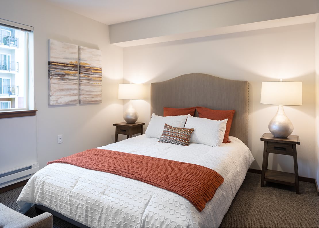 A modern and cozy bedroom with a neatly made bed, two side tables with lamps, and soothing wall art.
