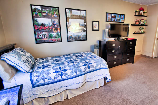 A cozy bedroom with a single bed featuring a blue quilt, a dresser with a TV on top, and wall posters.
