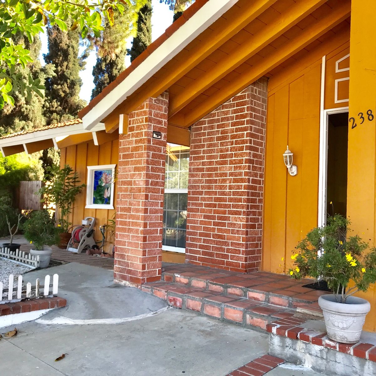 A welcoming house entrance with brick pillars and a small porch adorned with potted plants.