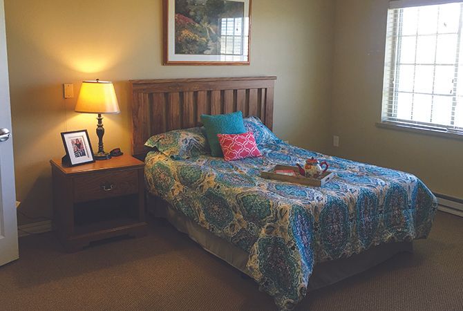 A cozy bedroom with a wooden bedframe, colorful bedding, and a nightstand with a lamp.
