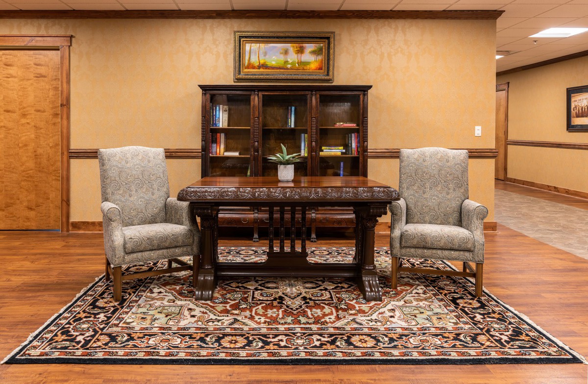 A well-furnished office with a wooden desk, two comfortable chairs, a bookshelf filled with books, and a decorative rug.