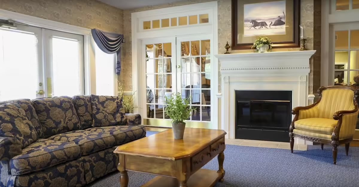 A cozy living room featuring a patterned sofa, wooden coffee table with a potted plant, and an elegant fireplace.