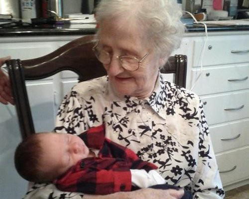 An elderly woman joyfully holds a sleeping baby indoors.