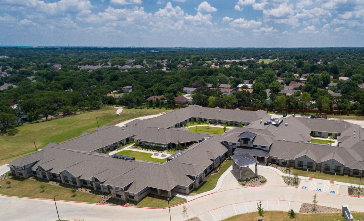 Aerial view of a large building complex surrounded by greenery and under a partly cloudy sky.