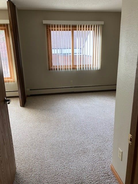 An empty room with carpet flooring and large windows letting in natural light.
