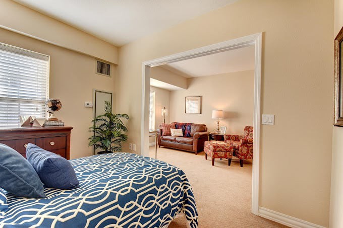 A cozy bedroom with a view of an adjoining living area, featuring comfortable furniture and warm decor.