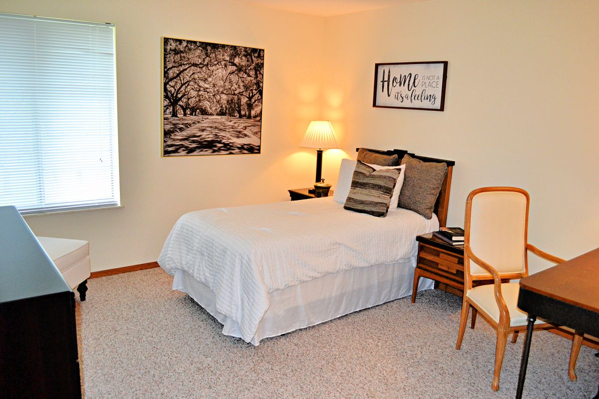 A cozy bedroom with a neatly made bed, decorative pillows, warm lighting, and wall art.
