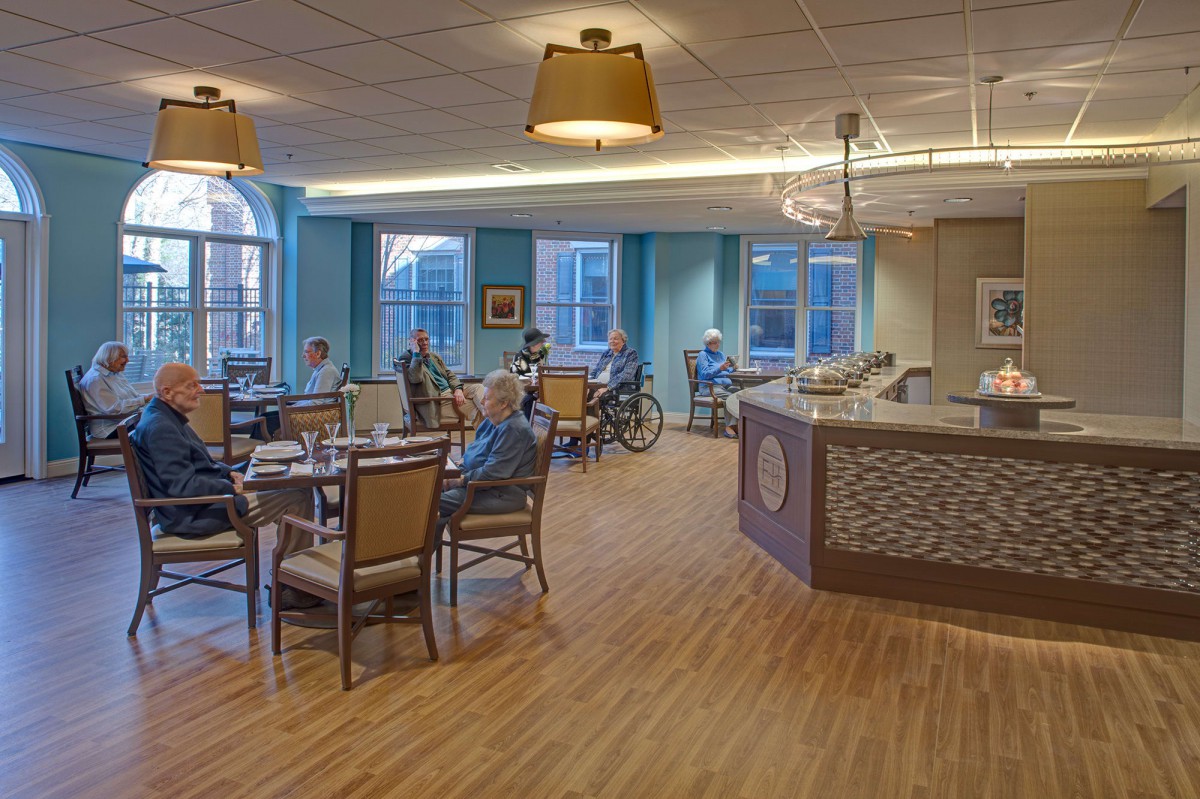 A cozy dining area in a senior living facility with tables, chairs, and people enjoying their meals.