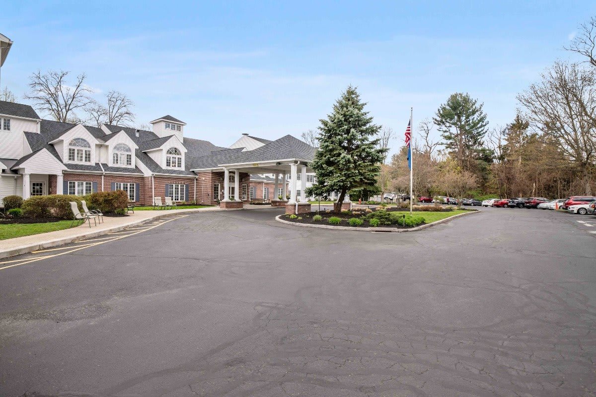 A large residential building surrounded by trees with a driveway leading to the entrance.