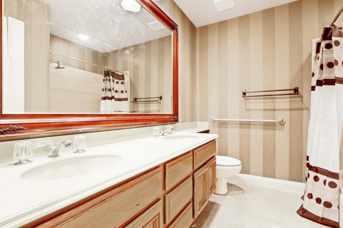 A spacious bathroom with a large mirror, wooden cabinets, and striped wallpaper.