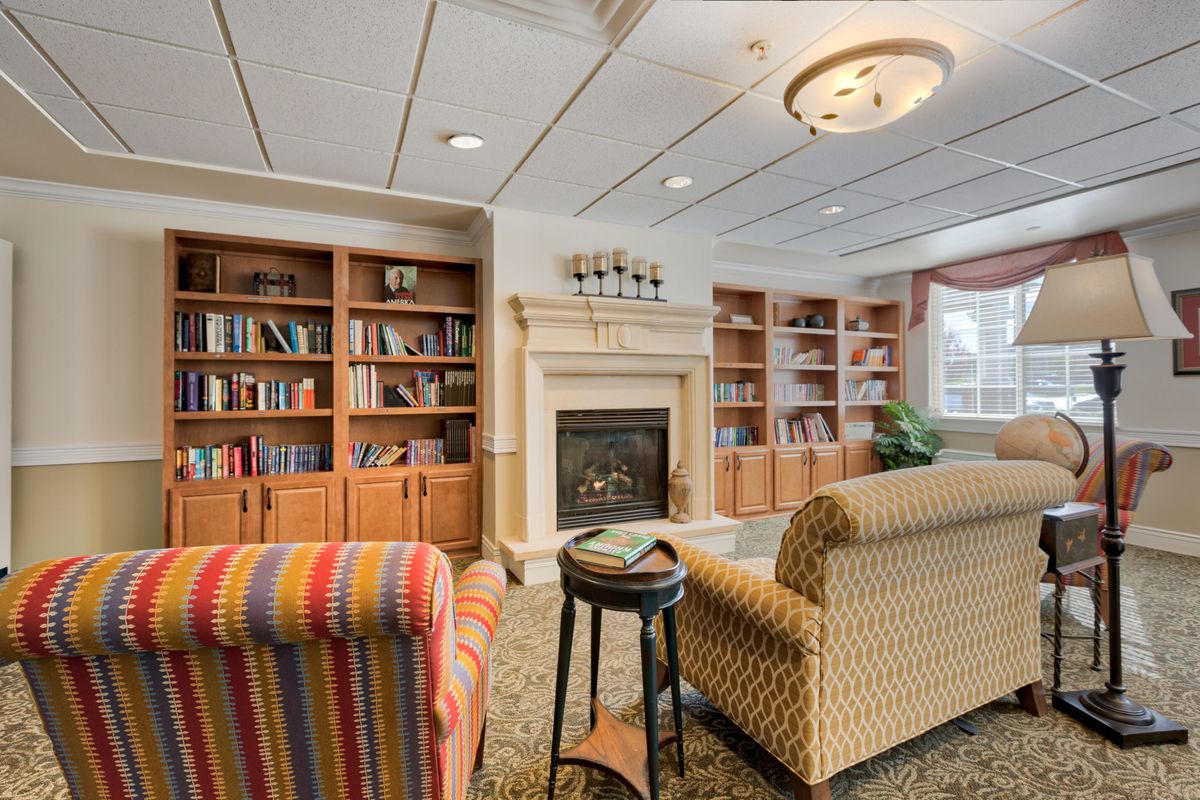 A cozy library reading room with comfortable armchairs and a fireplace surrounded by bookshelves.