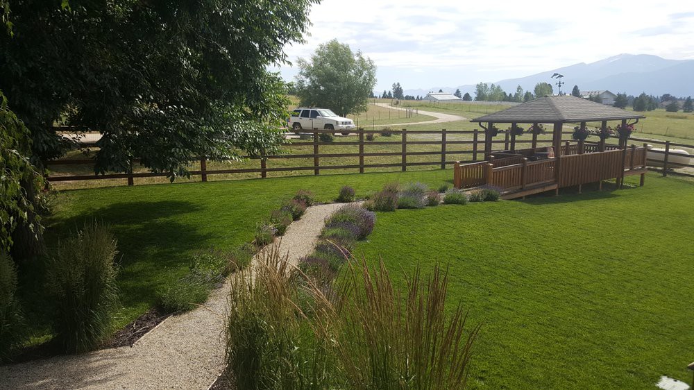 A well-maintained garden with a grassy lawn, pathway, and wooden fence in a rural setting.