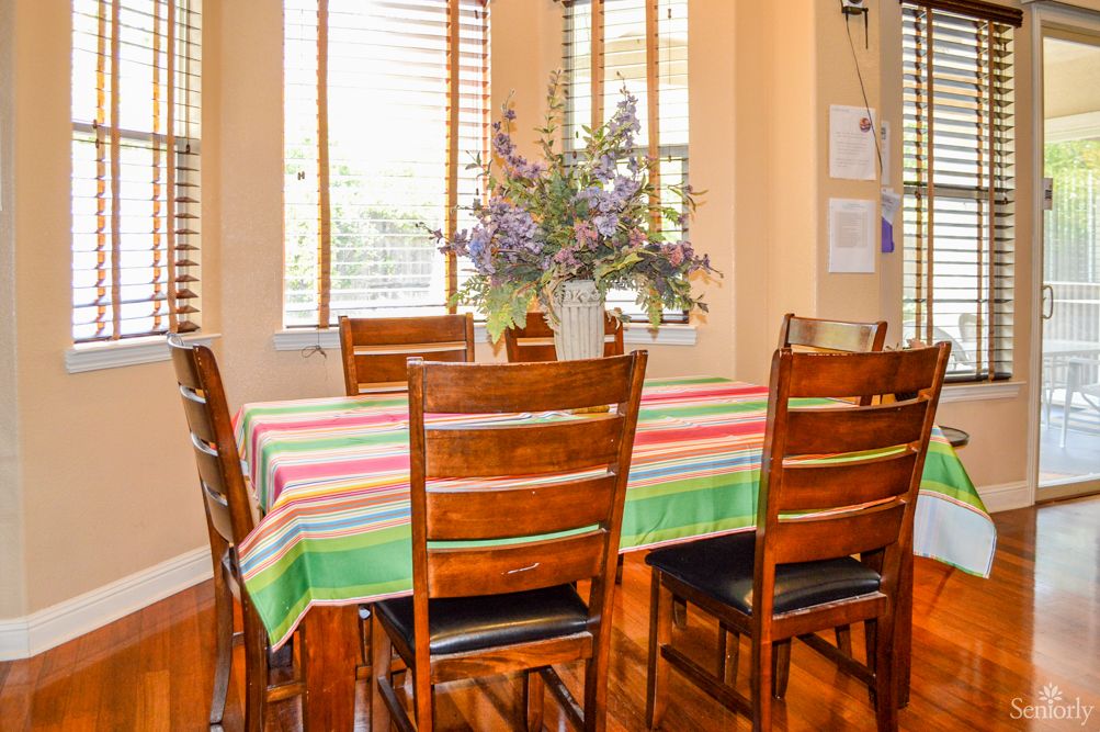 A cozy dining room with a colorful tablecloth and a bouquet of flowers on the table.